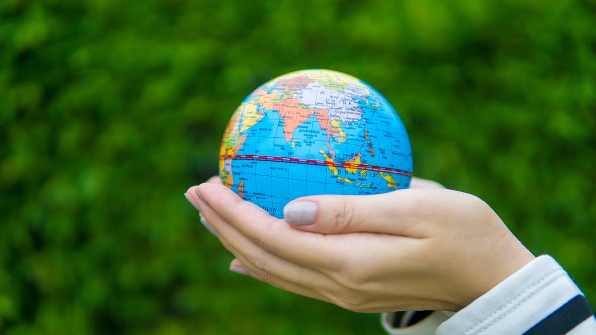 Close-up of hands gently cradling a miniature globe against a green backdrop.