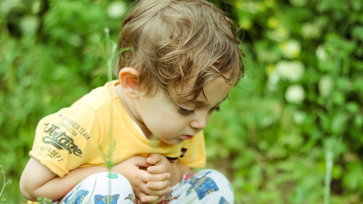 A young boy crouching and exploring nature in a grassy field.