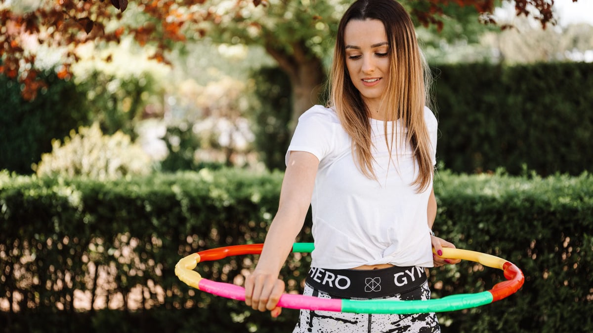 A fit woman enjoying a hula hoop workout in a sunny garden setting.